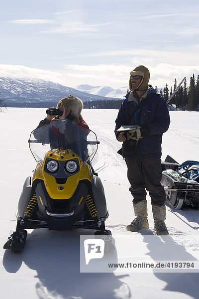 Hunters looking for game through binoculars while sitting on a snowmobile  skidoo  Yukon Territory  Canada  North America
