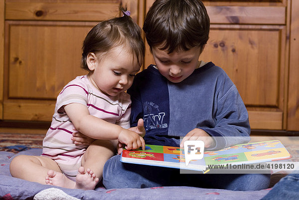 Vierjähriger Junge schaut mit seiner einjährigen Schwester ein Bilderbuch an.
