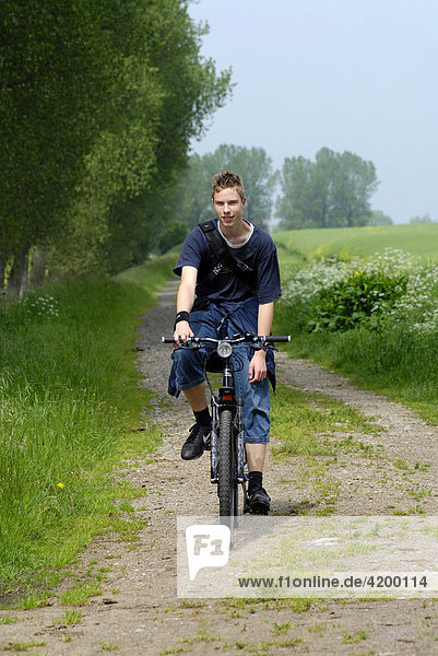 Teenager riding a bike on field path