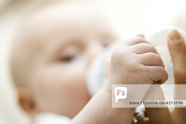 Baby trinkt aus der Flasche und hält den Finger der Mutter  Nahaufnahme
