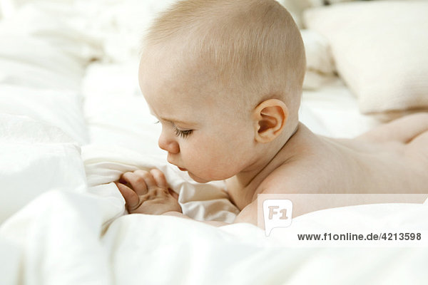 Baby auf dem Bett liegend  mit Blick auf die Finger
