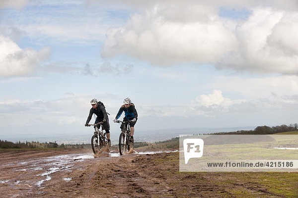 Couple riding mountain bikes through mud