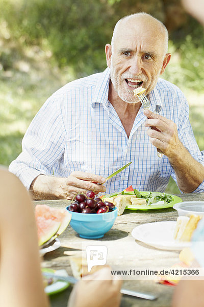 Älterer Mann beim Essen am Picknicktisch