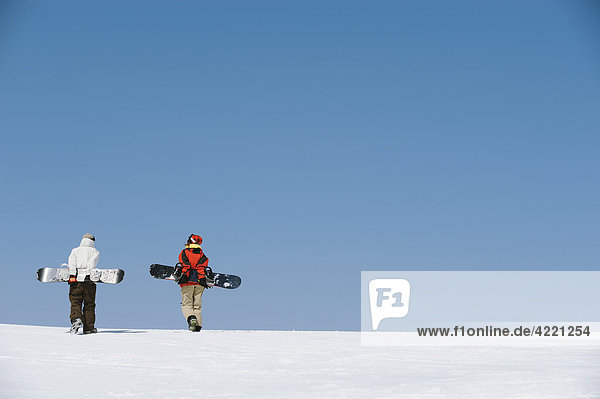 Paar zu Fuß auf Schneefeld hält Snowboards