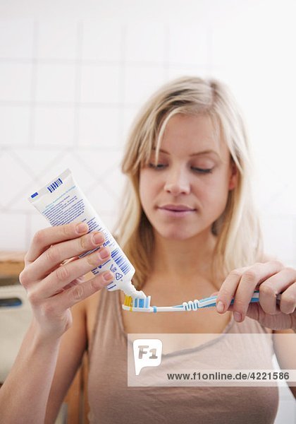 Frau im Bad stehend mit Zahnpasta und Zahnbürste