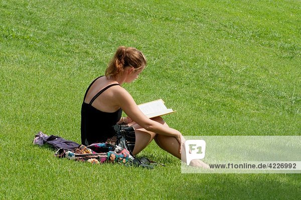 Young woman sitting on the grass  reading a book.