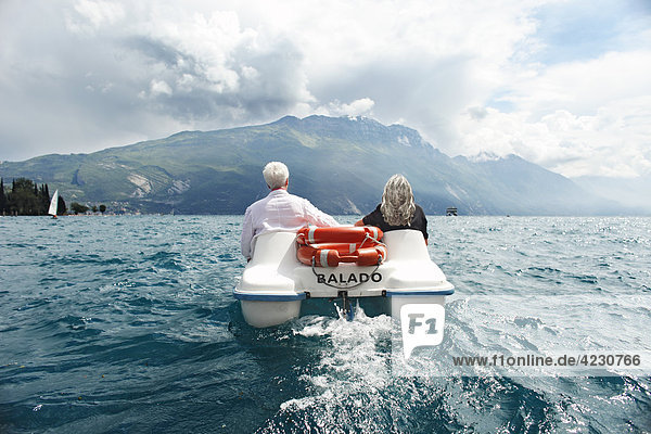 Seniorenpaar mit Tretboot vor Berglandschaft  Italien  Riva del Garda  Gardasee