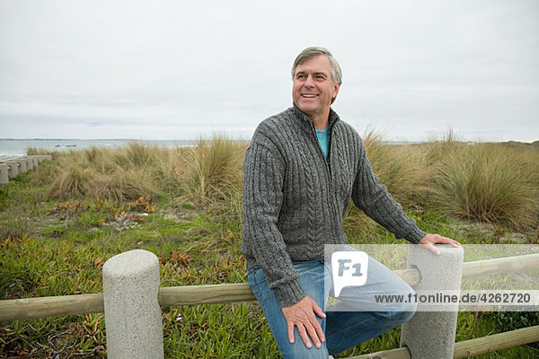 Mann auf einem Zaun an der Küste sitzend