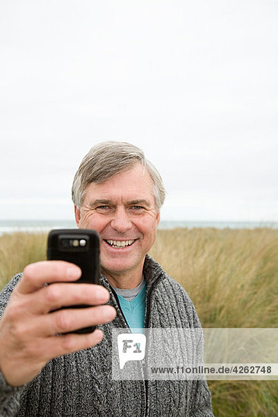 Mann an der Küste mit Fotohandy