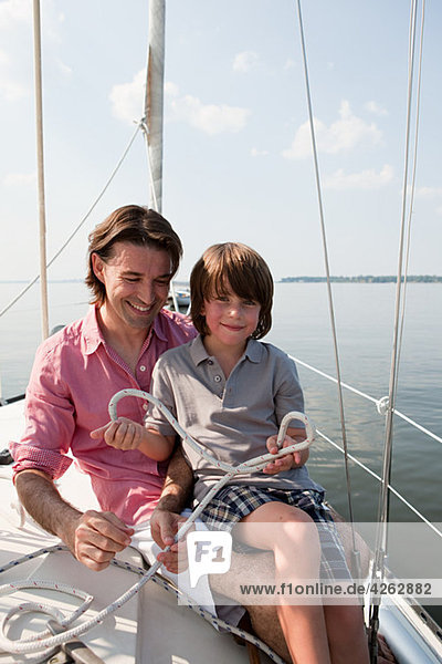 Father and son on board yacht holding rope