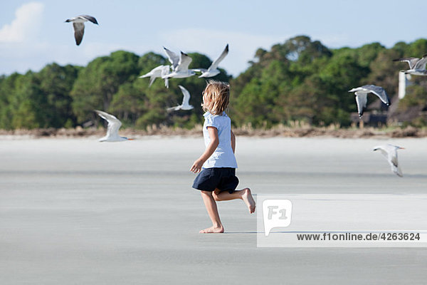 Girl running on beach amongst seagulls