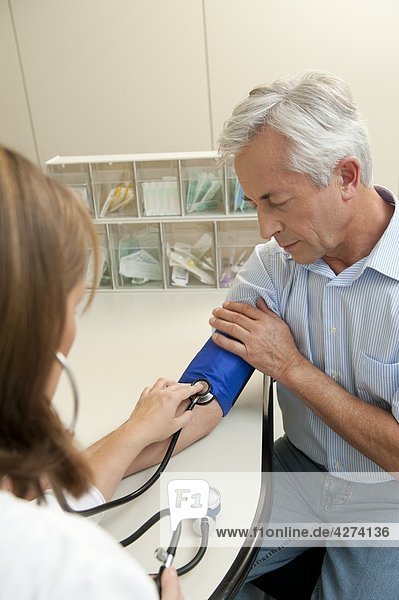 Ärztin misst bei einem Patienten den Blutdruck