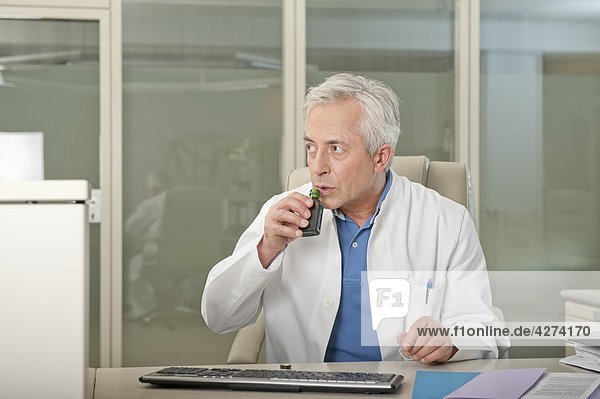 Arzt am Schreibtisch trinkt heimich Schnaps
