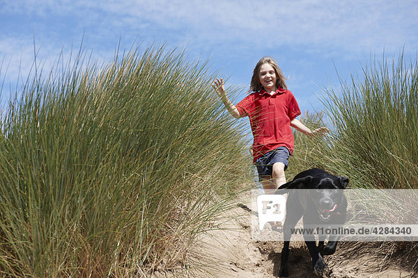 Junges Mädchen jagt Hund in Sanddünen