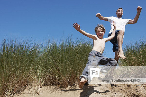 Vater und Sohn springen in Sanddünen