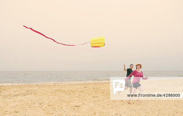 Happy couple fly kite on beach
