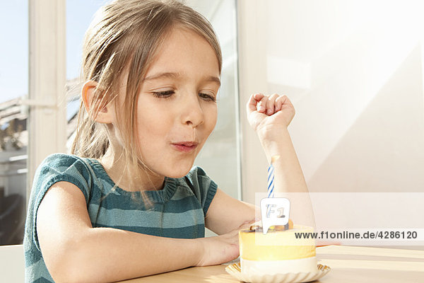 Mädchen bläst Kerze auf Geburtstagskuchen aus