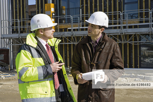 Geschäftsmann mit Schutzhelm und reflektierender Kleidung im Gespräch mit dem Bauunternehmer