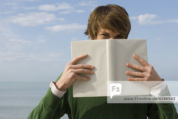 Young male holding book in front of face  portrait