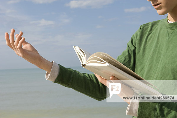 Junger Mann liest laut aus einem Buch am Strand vor