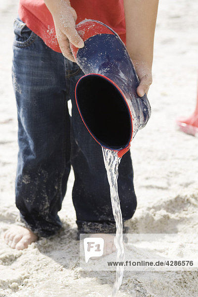 Kind schüttet Wasser aus dem Gummistiefel am Strand aus