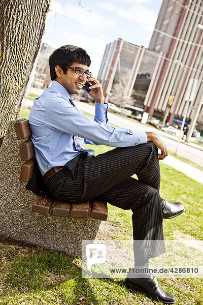 Businessman sitting auf Bank aus Seite  sprechen auf Handy