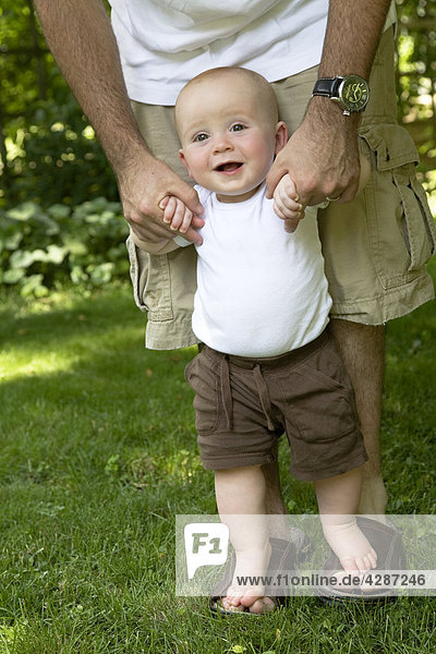 Baby boy standing on his Dad's feet while learning to walk  Ontario
