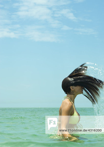 Frau  die im Meer steht und nasse Haare umdreht.