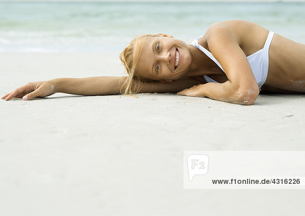 Frau am Strand liegend,  lächelnd vor der Kamera