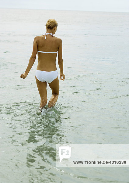 Frau im Bikini  knietief im Wasser  Rückansicht