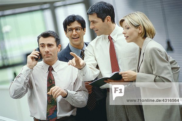 Four business colleagues standing in a group  one using phone  others listening