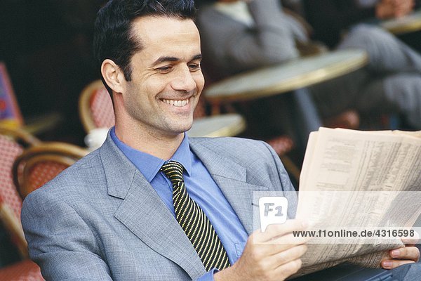 Geschäftsmann sitzt im Straßencafé  liest Finanzseiten  lächelt