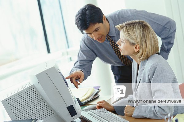 Businessman leaning over female colleague's shoulder pointing at monitor