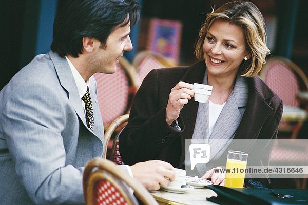 Geschäftsmann und Frau sitzen auf dem Bürgersteig und trinken Kaffee.