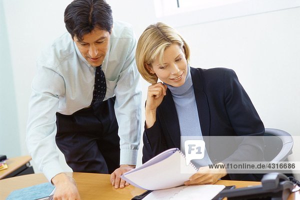 Business colleagues  man leaning over woman's shoulder  pointing to documents