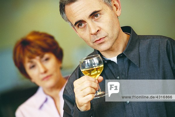 Älterer Mann mit einem Glas Wein  ältere Frau schaut ihn im Hintergrund an.