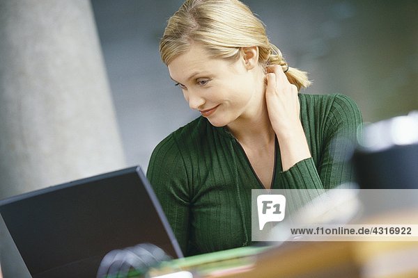 Young woman using laptop  smiling  hand behind neck