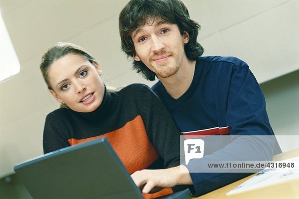 Couple using laptop  looking at camera