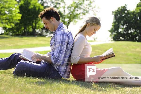 Couple sitting back to back reading in park