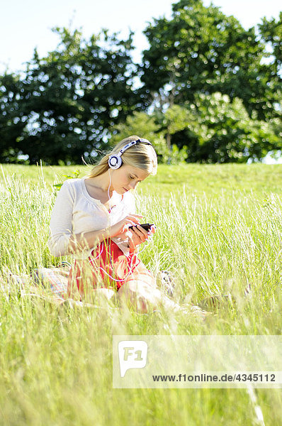 Junge Frau sitzt im hohen Gras und hört Kopfhörer.