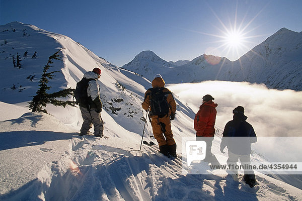 Backcountry heli-skiers stand atop ridge above clouds Chugach Mountains SC Alaska Winter near Girdwood