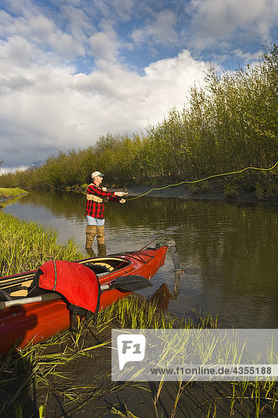 Man fly fishing on Rabbit Slough next to a lake kayak in Southcentral Alaska during summer