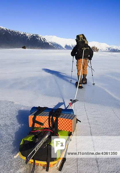 View of man pulling a gear laden sled into 40mph winds on the Stikine River near Point Rothsay  Stikine-LeConte Wilderness  Tongass National Forest  Winter  Southeast  Alaska