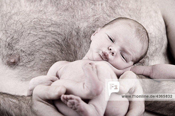 Close up of sleeping newborn infant being held against a man's bare chest nesteled in his arms Alaska United States