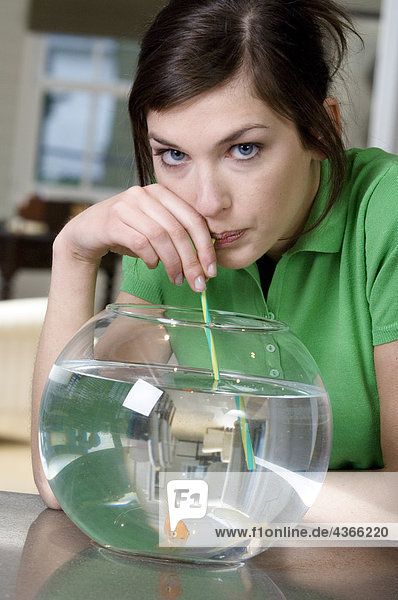 Junge Frau trinkt Aquarienwasser mit Strohhalm