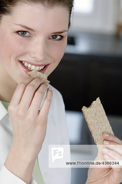 Porträt einer jungen Frau beim Essen eines Diätkekses
