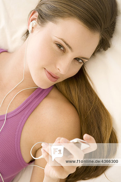 Junge Frau auf dem Bett liegend  Musik hörend