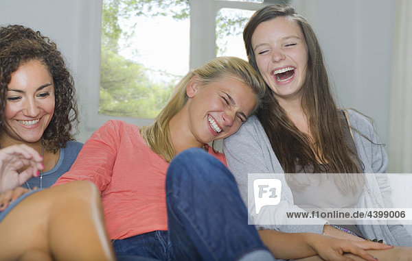 Junge Frauen lachen gemeinsam auf der Couch.