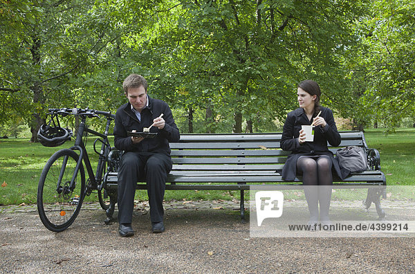 Woman and man eating lunch on park bench