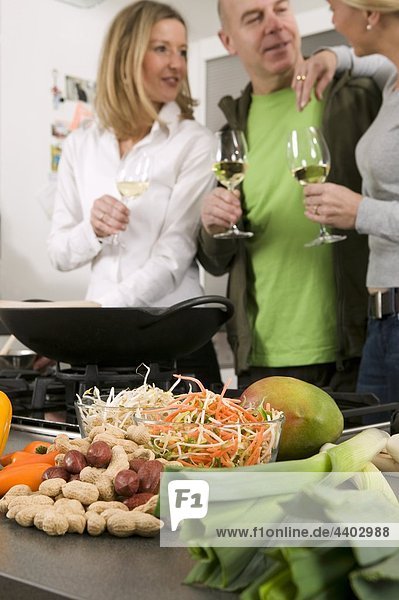 Mann und zwei Frauen mit Gläser Wein in Küche